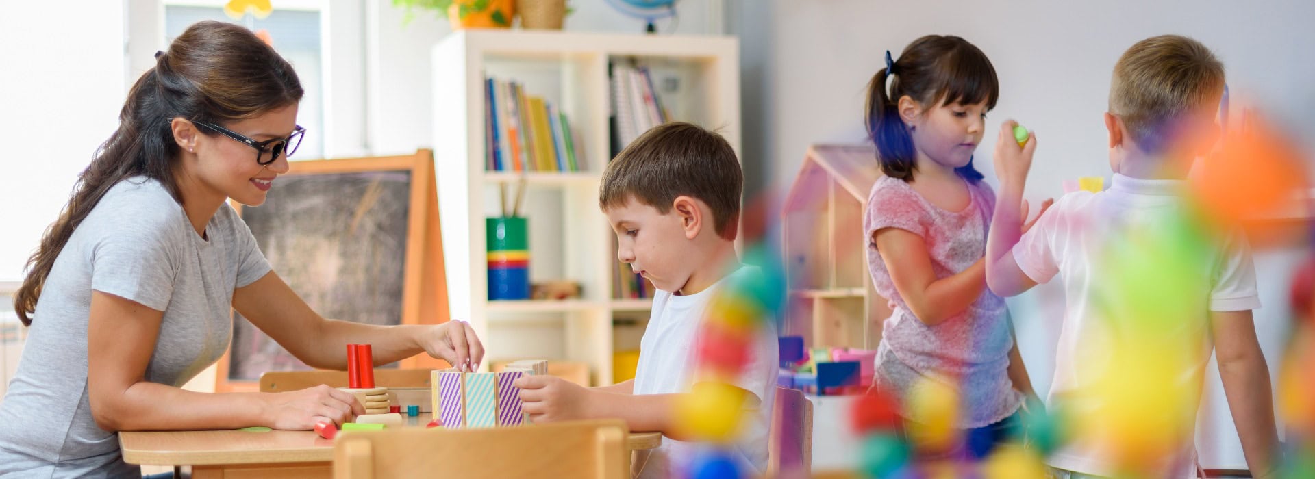 Erzieherin mit Kindern, die mit bunten Holzfiguren spielen