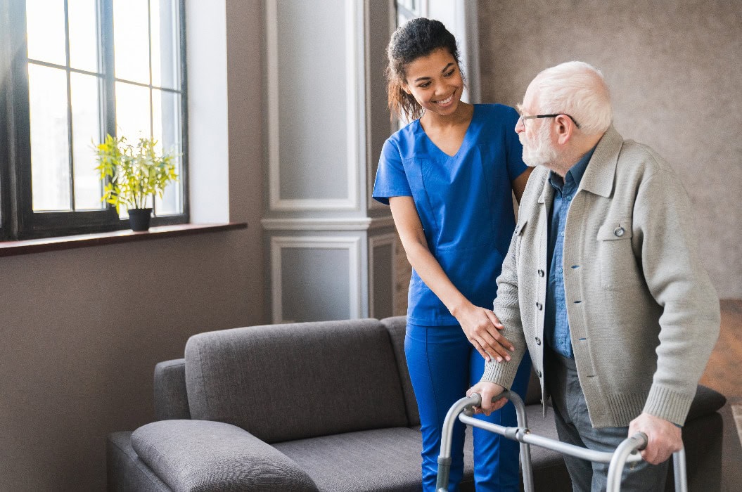 Älterer Patient eines Pflegeheims bewegt sich mit Gehhilfe und Unterstützung einer Krankenschwester